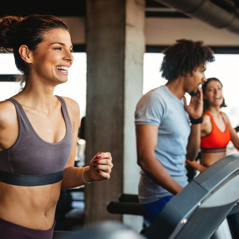 A busy gym parallax view of people exercising on treadmills while smiling.