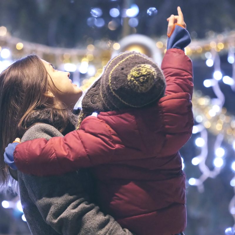 Portrait of mother holding child in her arms and admiring Christmas tree outdoors